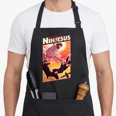 Tablier de cuisine noir avec illustration Ninjesus ninja Jésus et adversaires en tenues noires sur fond orange dégradé.