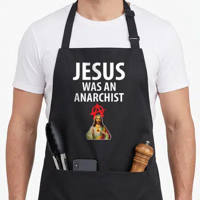 Tablier de cuisine noir avec l'inscription Jésus Was an Anarchist et une illustration de Jésus sous un signe A rouge.