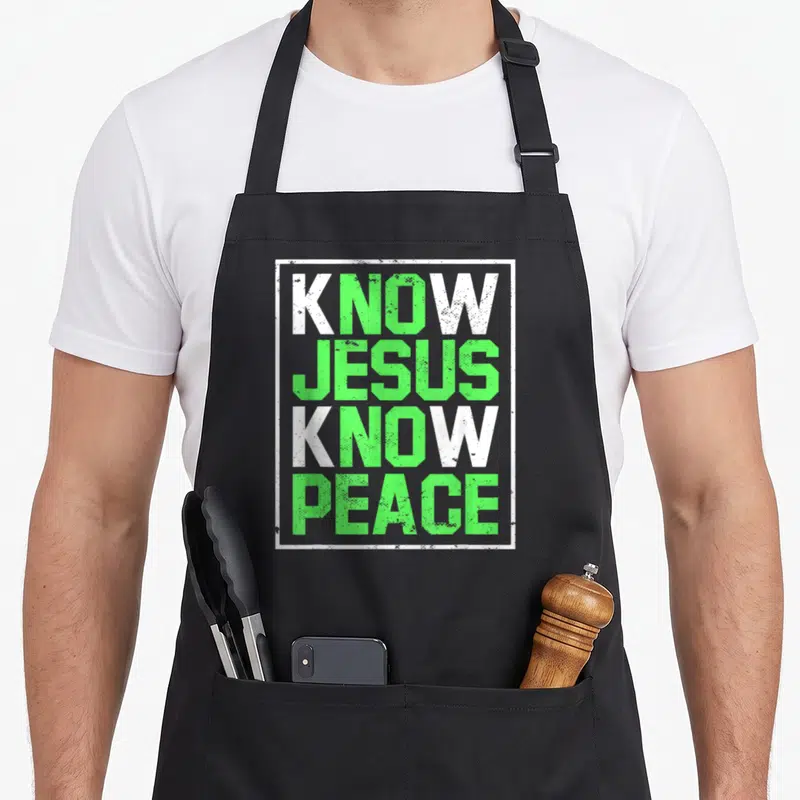 Tablier de cuisine noir avec l'inscription Know Jesus Know Peace en vert et blanc dans un cadre rectangulaire.