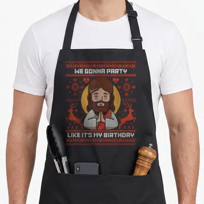 Tablier de cuisine noir avec illustration pixelisée de Jésus et texte blanc sur fond de motifs rouges de Noël.