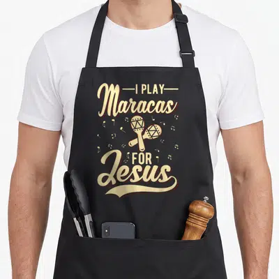Tablier de cuisine noir avec inscription beige « I Play Maracas For Jesus » et deux maracas croisés entourés de notes de musique.