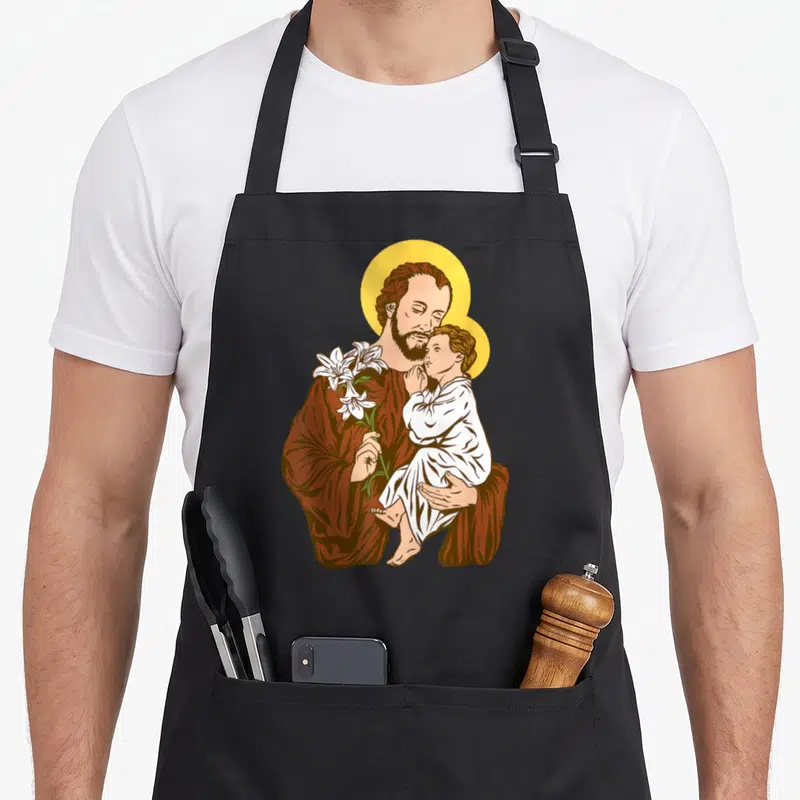 Tablier de cuisine noir avec illustration colorée de Saint Joseph tenant l'Enfant Jésus et un lys blanc sous un halo doré.