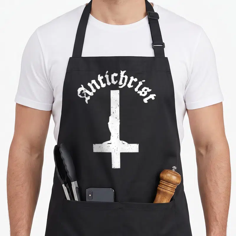 Tablier de cuisine noir avec inscription Antichrist et croix blanche inversée texturée sur le devant.