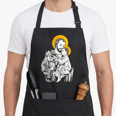 Tablier de cuisine noir avec illustration blanche de Saint Joseph tenant l'Enfant Jésus et un lys, sur fond de halo doré.