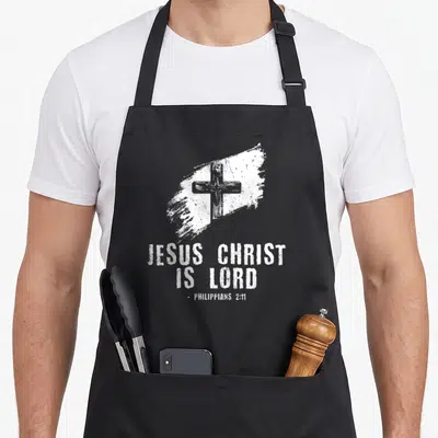 Tablier de cuisine noir avec inscription Jésus Christ est Seigneur et une croix blanche sur un trait de peinture.
