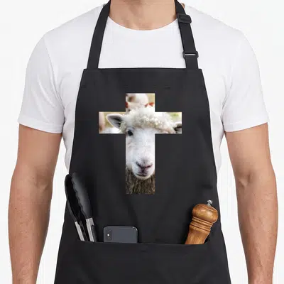Tablier de cuisine noir avec un agneau blanc dont la tête forme une croix.
