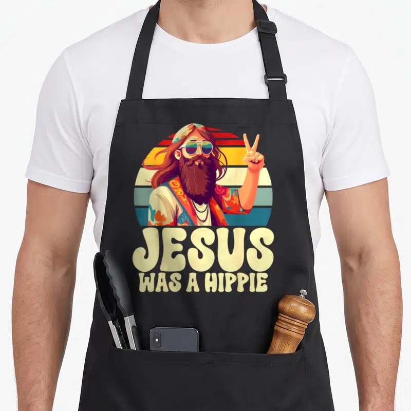 Tablier de cuisine noir avec illustration d'un Jésus hippie aux longs cheveux et texte Jesus was a hippie en dessous.