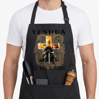 Tablier de cuisine noir avec illustration d'un croisé, une croix orange et les mots Yeshua The King Is Coming.