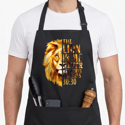 Tablier de cuisine noir avec tête de lion dorée et texte The Lion In Me Never Retreats Proverbs 30:30