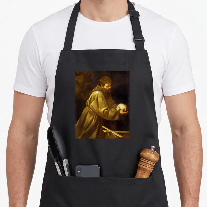 Tablier de cuisine noir avec reproduction du tableau Saint François en prière par Caravage, montrant le saint tenant un crâne.