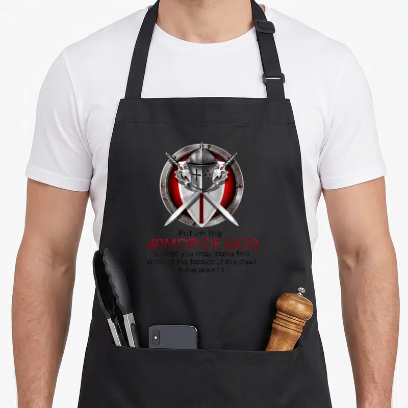 Tablier de cuisine noir avec casque, bouclier et sabres croisés sur fond rouge.