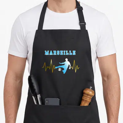 Tablier de cuisine noir avec inscription Marseille en bleu, silhouette de joueur et ligne ondulée dorée traversant la composition.