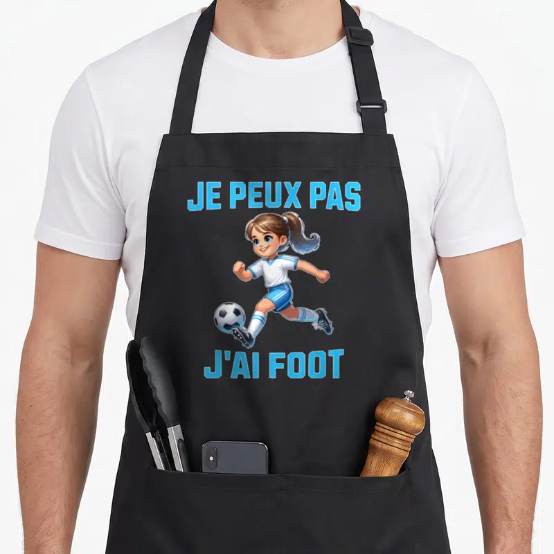 Tablier de cuisine noir avec une jeune fille jouant au football et le texte Je peux pas j'ai foot.