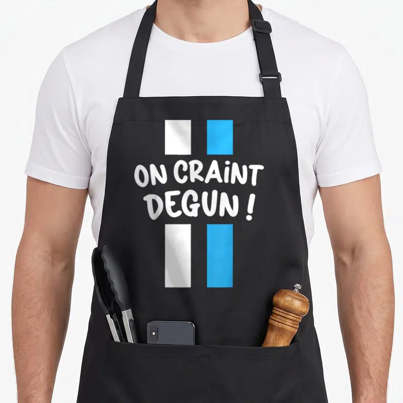 Tablier de cuisine noir avec une croix bleue et blanche et le texte On Craint Degun en lettres blanches capitales.