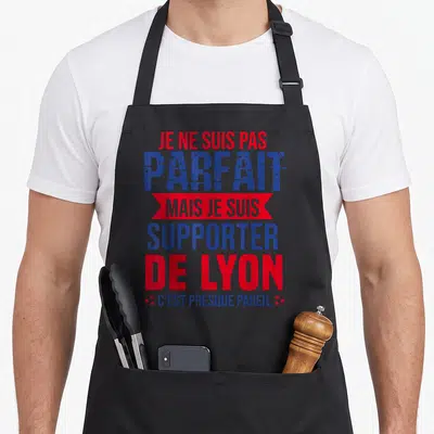 Tablier de cuisine noir avec le texte Je ne suis pas parfait mais je suis supporter de Lyon en bleu et rouge.