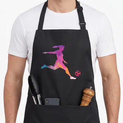 Tablier de cuisine noir avec silhouette artistique d'une joueuse de football aux couleurs vives frappeant un ballon rose