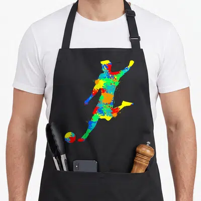 Tablier de cuisine noir avec une silhouette d'enfant jouant au football formée par des taches de peinture colorées vives.