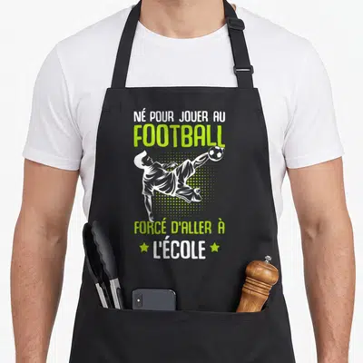 Tablier de cuisine noir avec illustration d'un footballeur et texte humoristique sur le football et l'école.