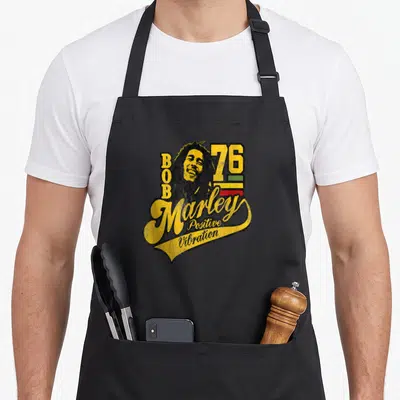 Tablier de cuisine noir avec illustration vintage de Bob Marley, le chiffre 76 et l'inscription Positive Vibration en jaune.