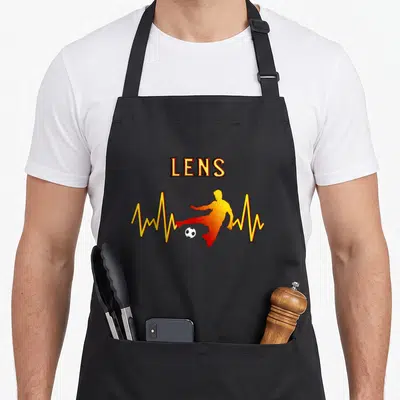 Tablier de cuisine noir avec silhouette orange frappant un ballon, ligne jaune et inscription LENS en lettres dorées.