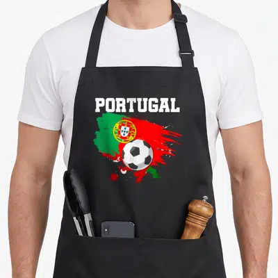 Tablier de cuisine noir avec illustration drapeau Portugal, ballon de foot et texte blanc PORTUGAL sur fond de taches.