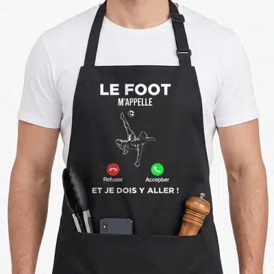 Tablier de cuisine noir avec illustration d'un footballeur effectuant un contre-la-vent et texte blanc sur fond uni.