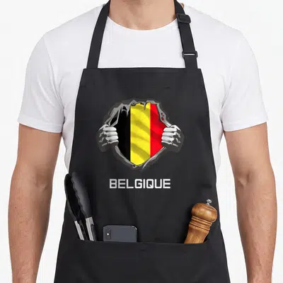 Tablier de cuisine noir avec illustration de mains déchirant un maillot revealing le drapeau belge et l'inscription BELGIQUE