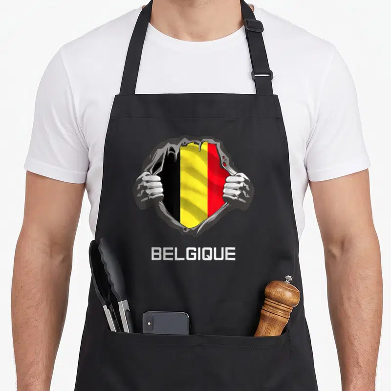 Tablier de cuisine noir avec illustration de mains déchirant un maillot revealing le drapeau belge et l'inscription BELGIQUE