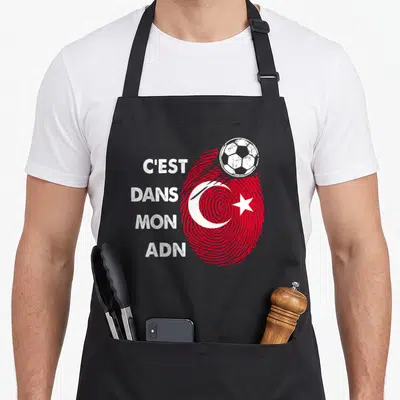 Tablier de cuisine noir avec une empreinte rouge formant le drapeau Turquie et un ballon de foot blanc posé dessus.