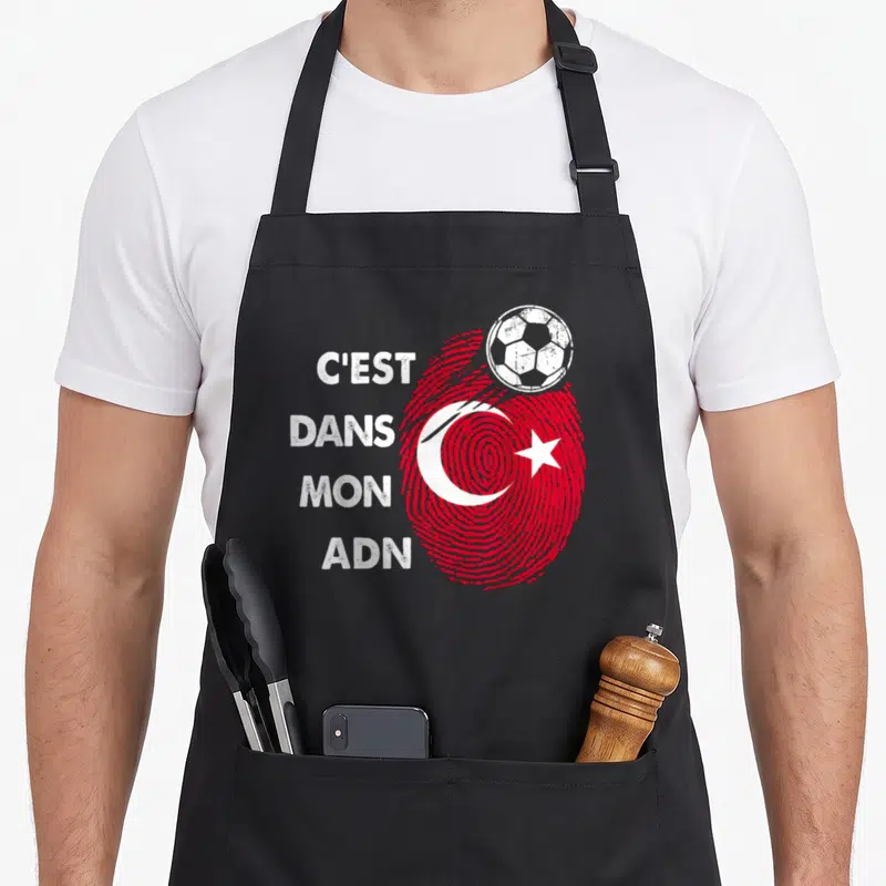 Tablier de cuisine noir avec une empreinte rouge formant le drapeau Turquie et un ballon de foot blanc posé dessus.