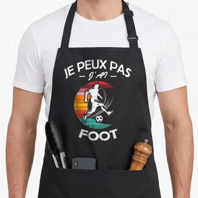 Tablier de cuisine noir avec inscription Je peux pas j'ai foot et silhouette de footballeur sur fond arc-en-ciel vintage.
