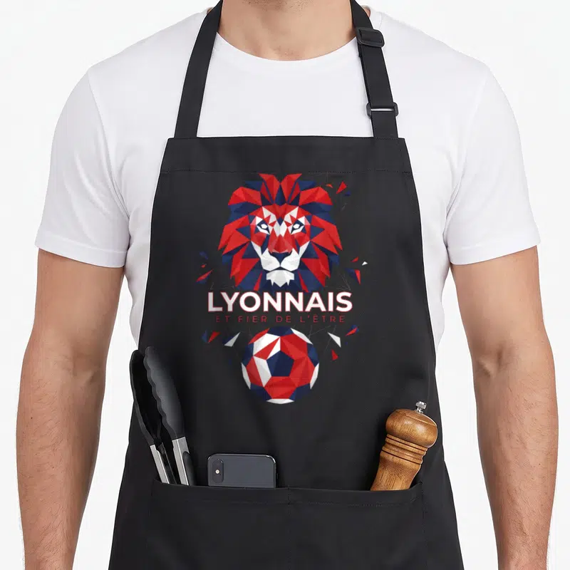 Tablier de cuisine noir avec tête de lion géométrique rouge et bleu et texte Lyonnais et fier de l'être au-dessus d'un ballon.