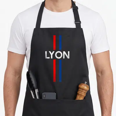 Tablier de cuisine noir avec inscription LYON et deux bandes verticales rouge et bleue sur fond uni.