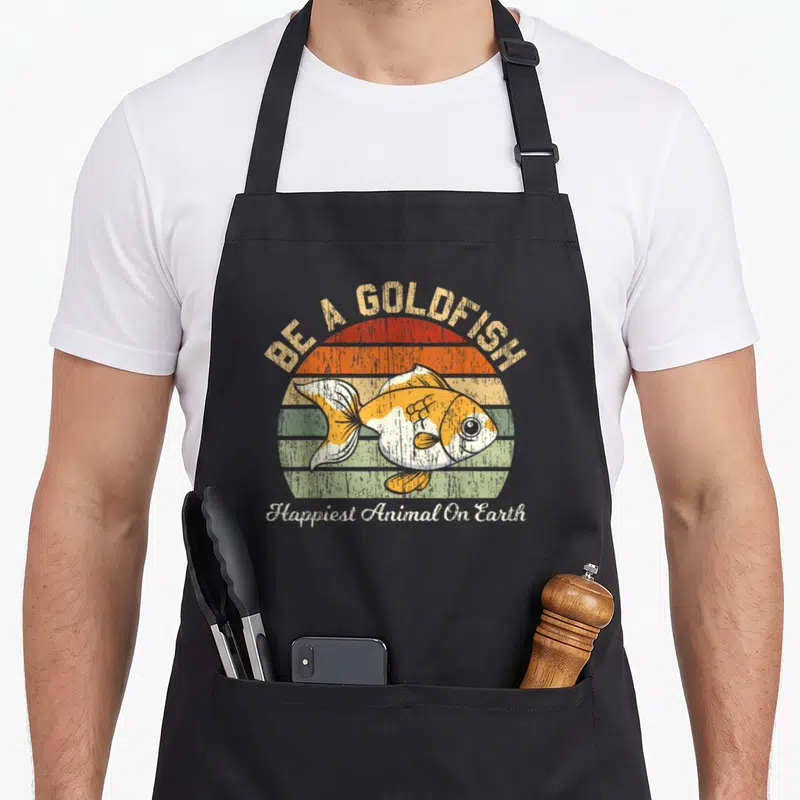 Tablier de cuisine noir avec illustration d'un poisson orange et blanc sur fond de soleil rayé multicolore.