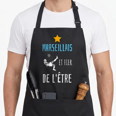 Tablier de cuisine noir avec un joueur de foot effectuant une frappe du pied et le texte Marseillais et fier de l'être.