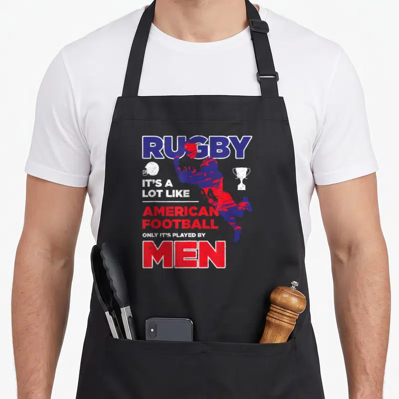 Tablier de cuisine noir avec illustration d'un joueur de rugby et texte humoristique en bleu et rouge.