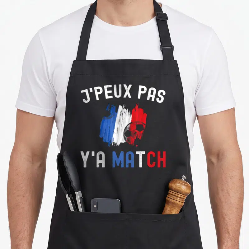 Tablier de cuisine noir avec inscription J'peux pas y'a match et drapeau français stylisé autour d'un ballon de foot.