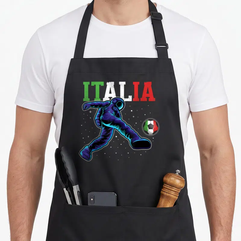 Tablier de cuisine noir avec illustration d'un astronaute frappant un ballon aux couleurs du drapeau italien sur fond étoilé.