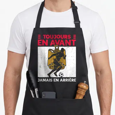 Tablier de cuisine noir avec inscription toujours en avant jamais en arrière et silhouette de footballeur sur aigle égyptien doré.