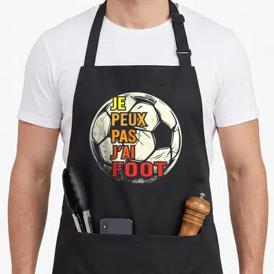 Tablier de cuisine noir avec un ballon de football blanc et le texte Je peux pas j'ai foot en lettres colorées.