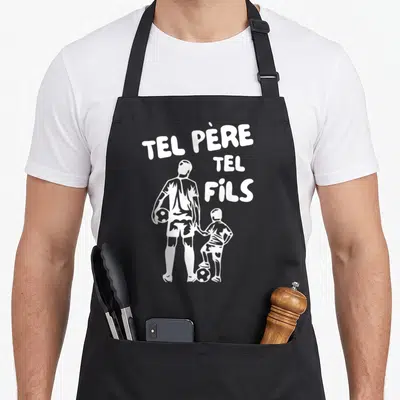 Tablier de cuisine noir avec une silhouette blanche d'un homme et d'un enfant tenant la main près d'un ballon de foot.