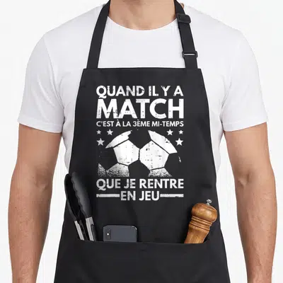 Tablier de cuisine noir avec inscription blanche humoristique sur le football et illustration de ballon délavé entouré d'étoiles.