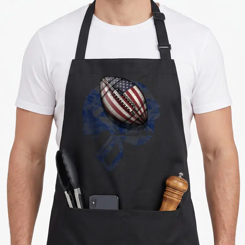 Tablier de cuisine noir avec une balle de football américaine au design du drapeau et un casque bleu en arrière-plan texturé.