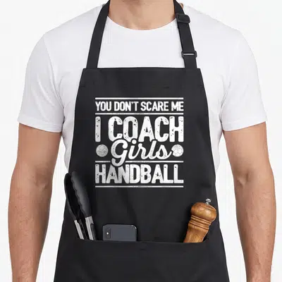 Tablier de cuisine noir avec inscription blanche I Coach Girls Handball et deux ballons de handball stylisés.