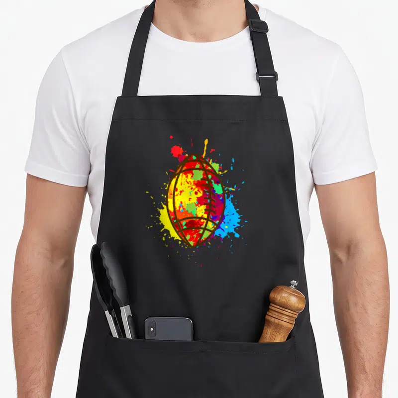 Tablier de cuisine noir avec ballon de rugby peint en couleurs vives et éclaboussures artistiques.