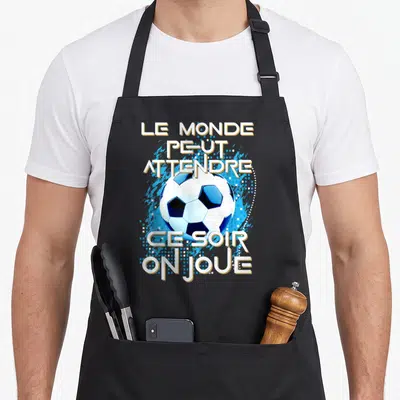 Tablier de cuisine noir avec un ballon de foot et le texte Le monde peut attendre ce soir on joue en bleu et blanc.