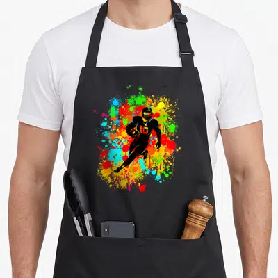 Tablier de cuisine noir avec joueur de football américain au maillot 10 et ballon entouré d'éclats de couleurs vives.