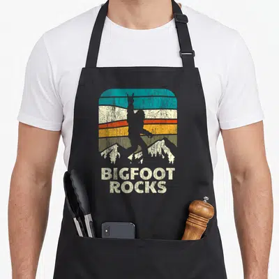 Tablier de cuisine noir avec silhouette Bigfoot et texte Bigfoot Rocks sur fond de montagnes colorées