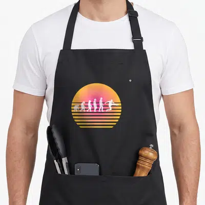 Tablier de cuisine noir avec illustration évolutive d'un joueur de foot sur fond de soleil rétro orange et jaune strié.