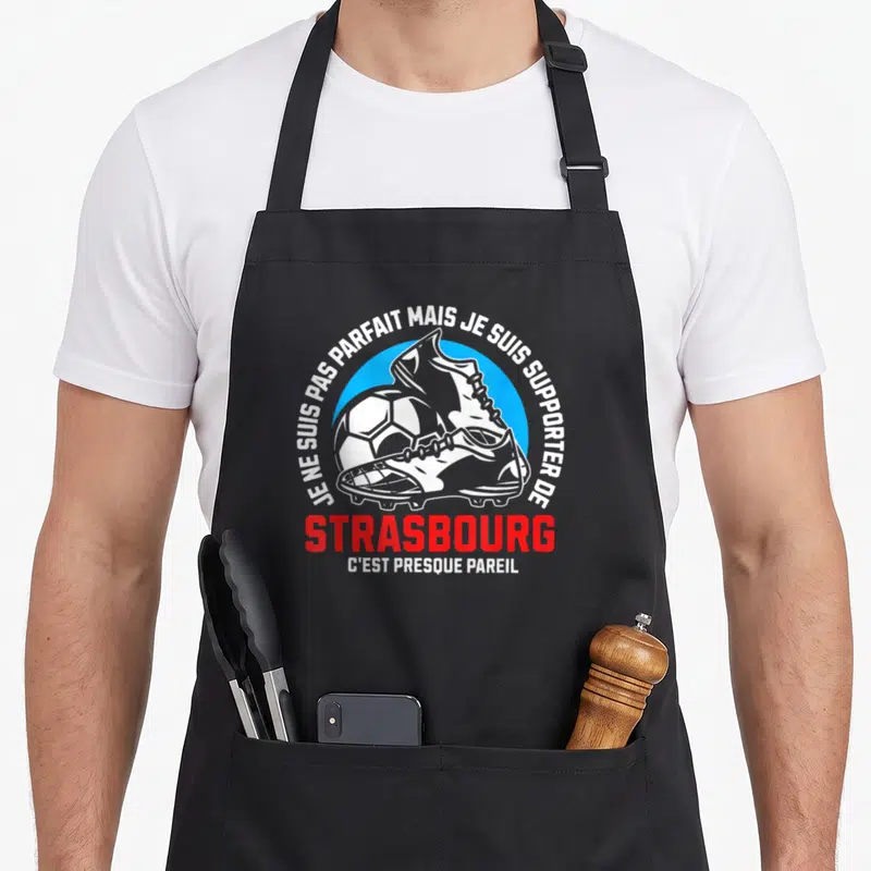 Tablier de cuisine noir avec illustration de bottines de foot et texte blanc et rouge sur fond bleu circulaire.
